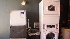 A compact laundry area with a washing machine, dryer, and a small trash bin. - Village Inn Cotulla (Cotulla)