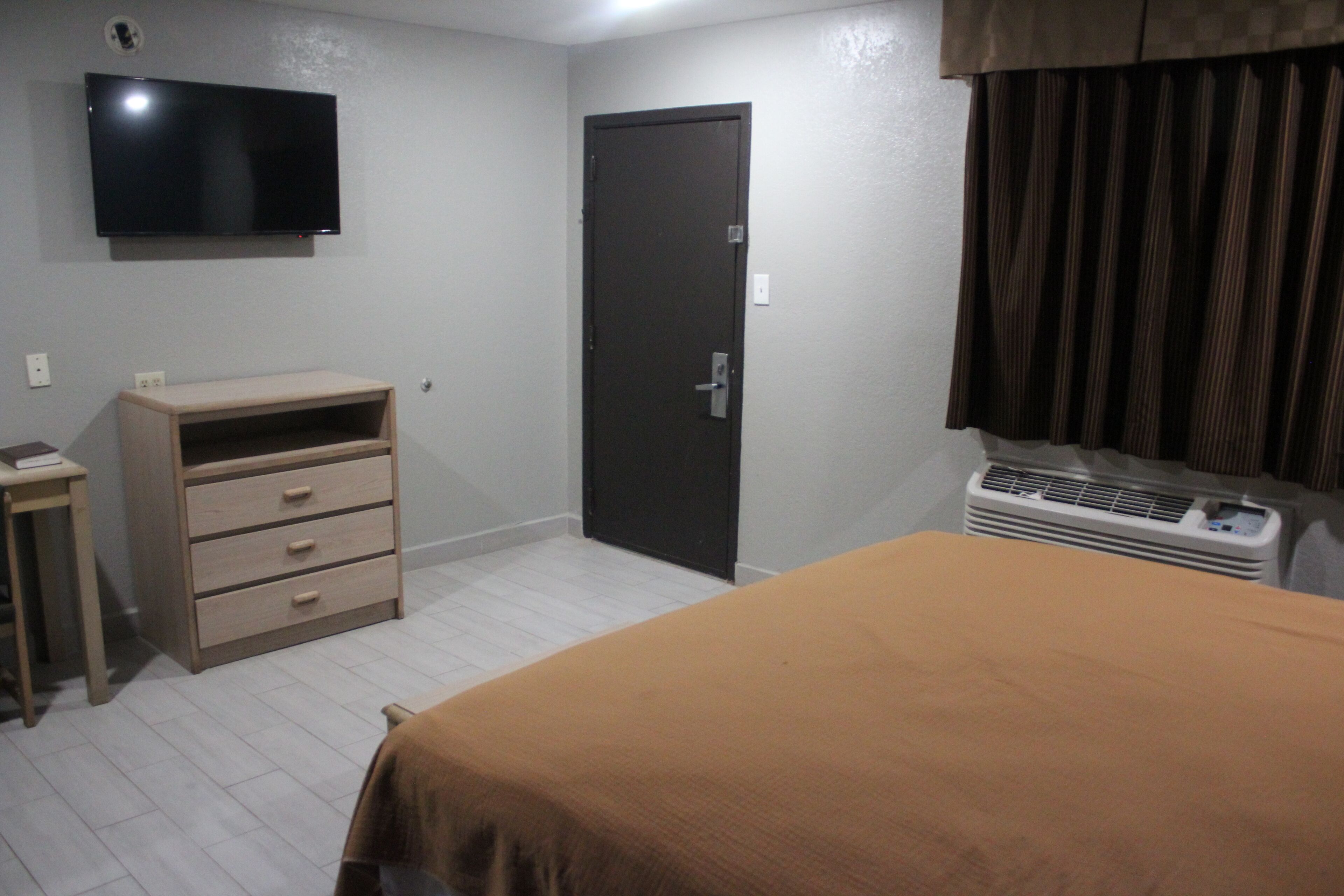 A bedroom with a bed, a dresser, a television, a door, and an air conditioning unit.