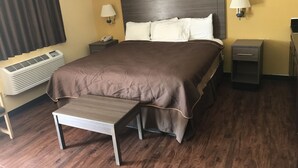A hotel room with a large bed, bedside lamps, a bedside phone, an air conditioner, a small table, and a nightstand. - Village Inn Cotulla (Cotulla)
