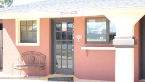 A building with a sign reading "OFFICE" above the entrance, a metal bench outside, and a door with a window. - Village Inn Cotulla (Cotulla)