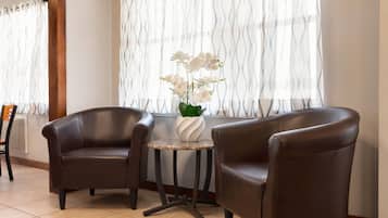 A room with two brown leather chairs, a small round table with a white vase of flowers, and a window with sheer curtains.