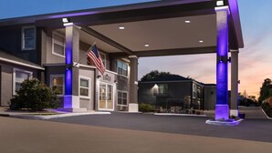 A hotel entrance with an American flag, a covered parking area, and a well-lit facade. - Days Inn by Wyndham Suites Fredericksburg (Fredericksburg)