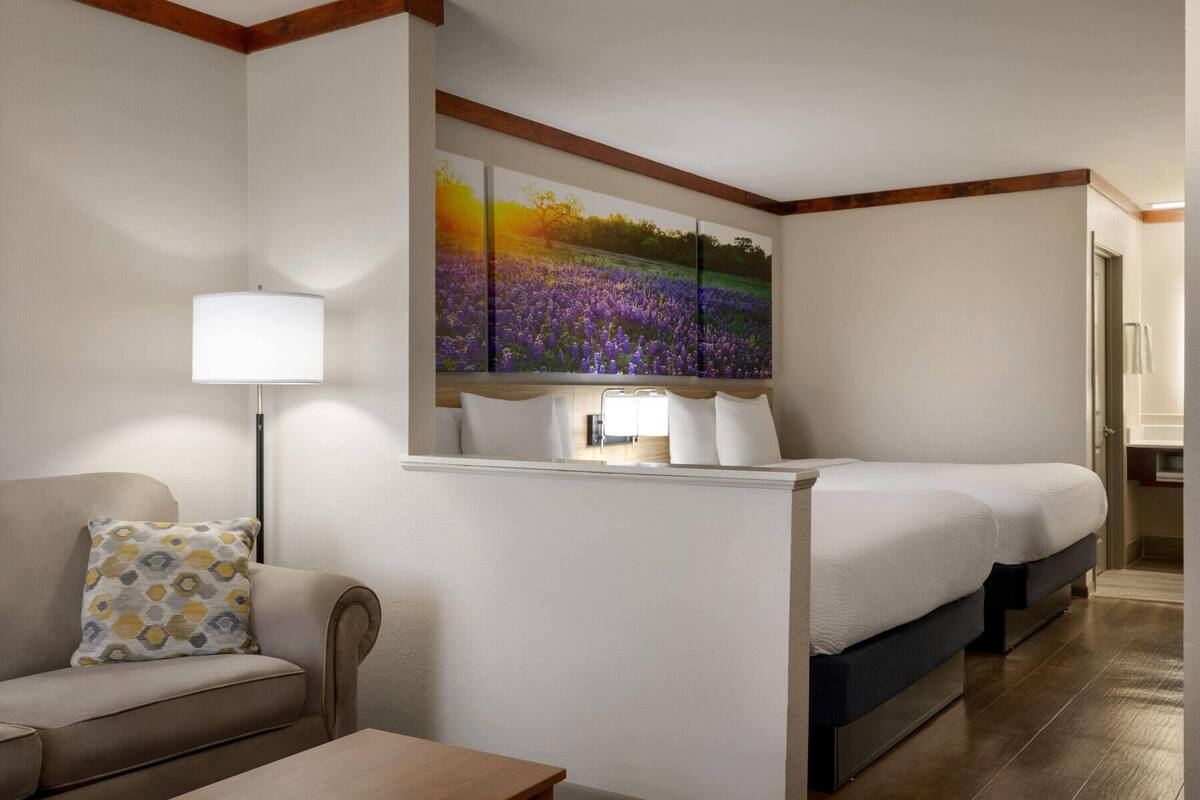 A hotel room with a sofa, a bed, a nightstand, a lamp, and a large painting on the wall.