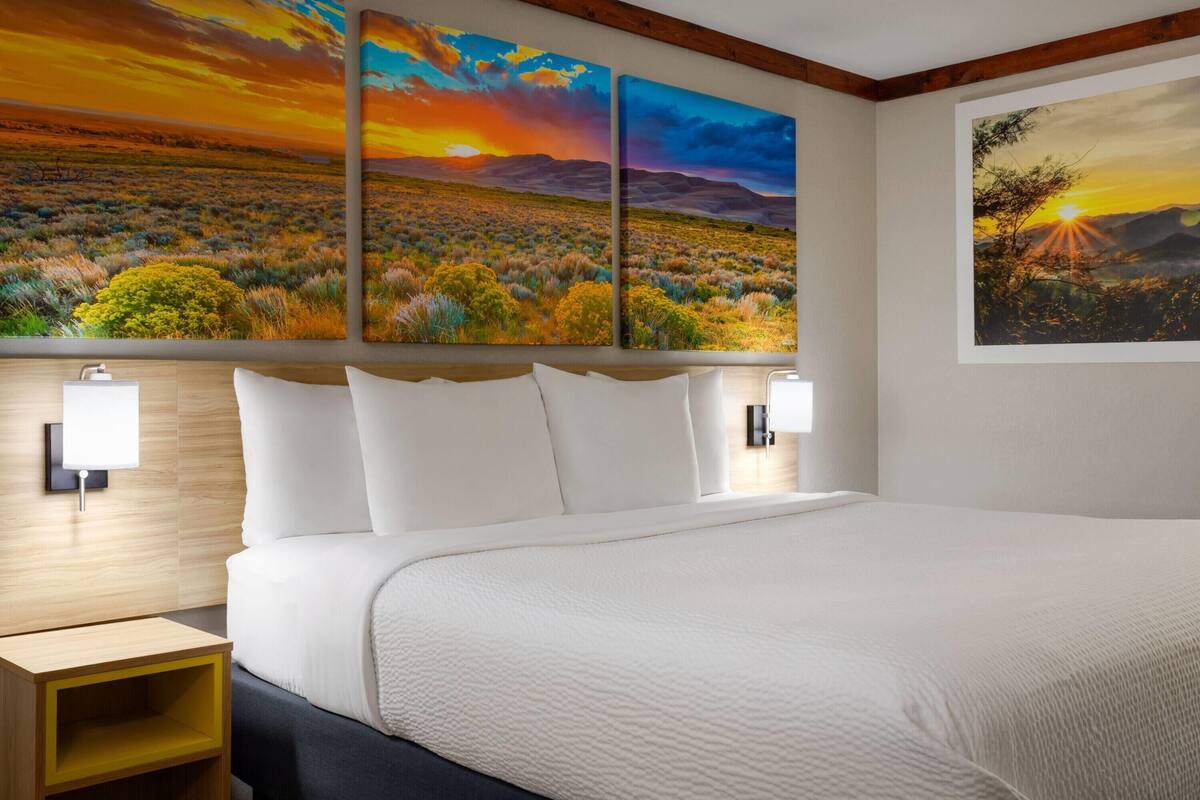 A hotel room with a large bed, two wall-mounted paintings of landscapes, and bedside lamps.