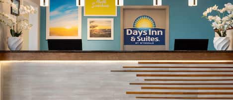 Un comptoir d’accueil avec une enseigne « Days Inn & Suites », des photos encadrées et des orchidées blanches.