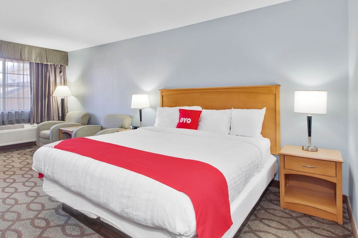 A hotel room with a large bed, two bedside tables with lamps, a chair, a desk, and a window with curtains.