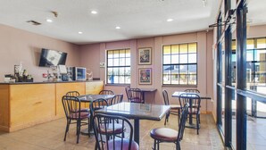 A restaurant interior with a bar area, multiple tables and chairs, and large windows providing natural light.