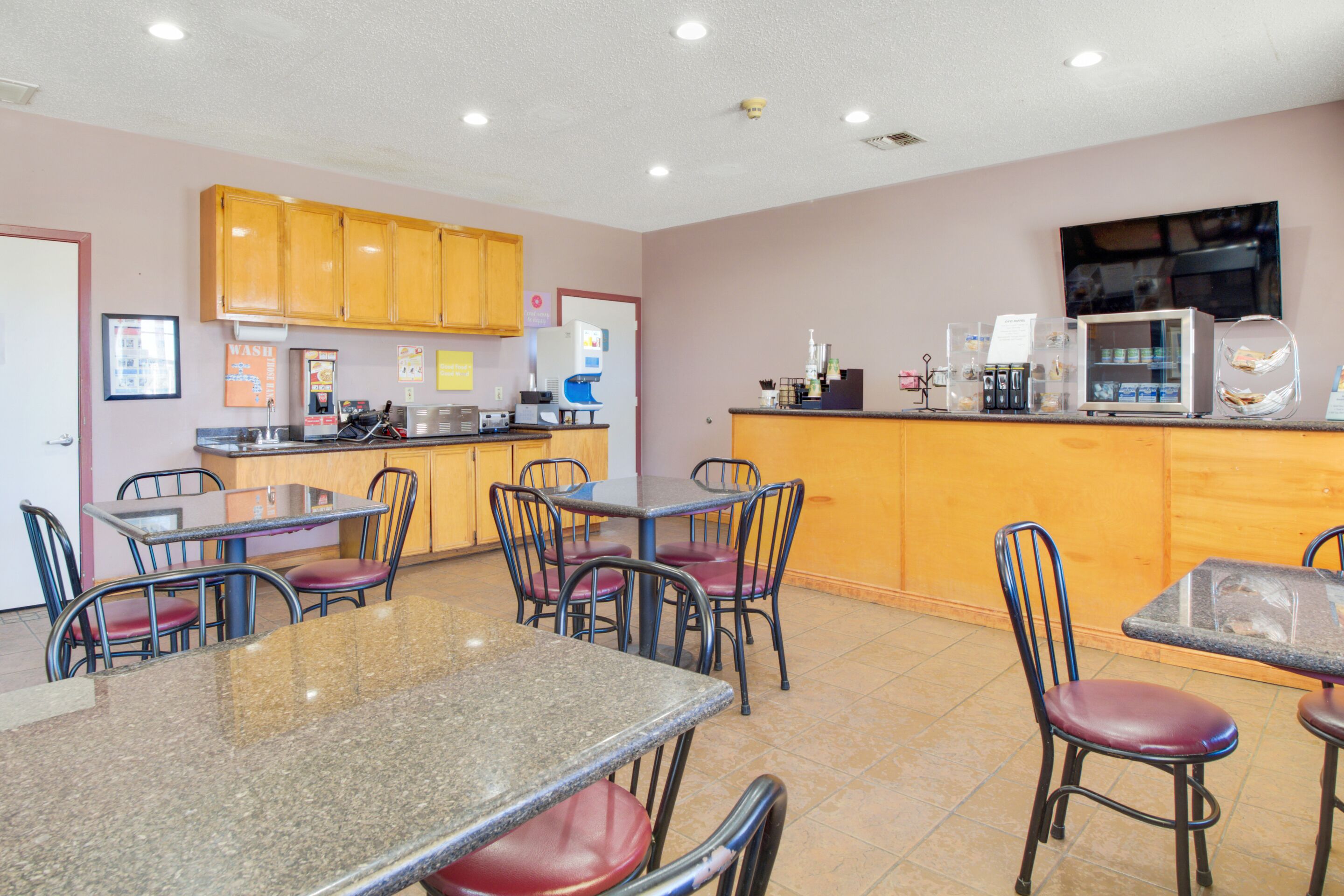 A restaurant with multiple tables and chairs, a kitchen area, and a counter with a coffee machine.