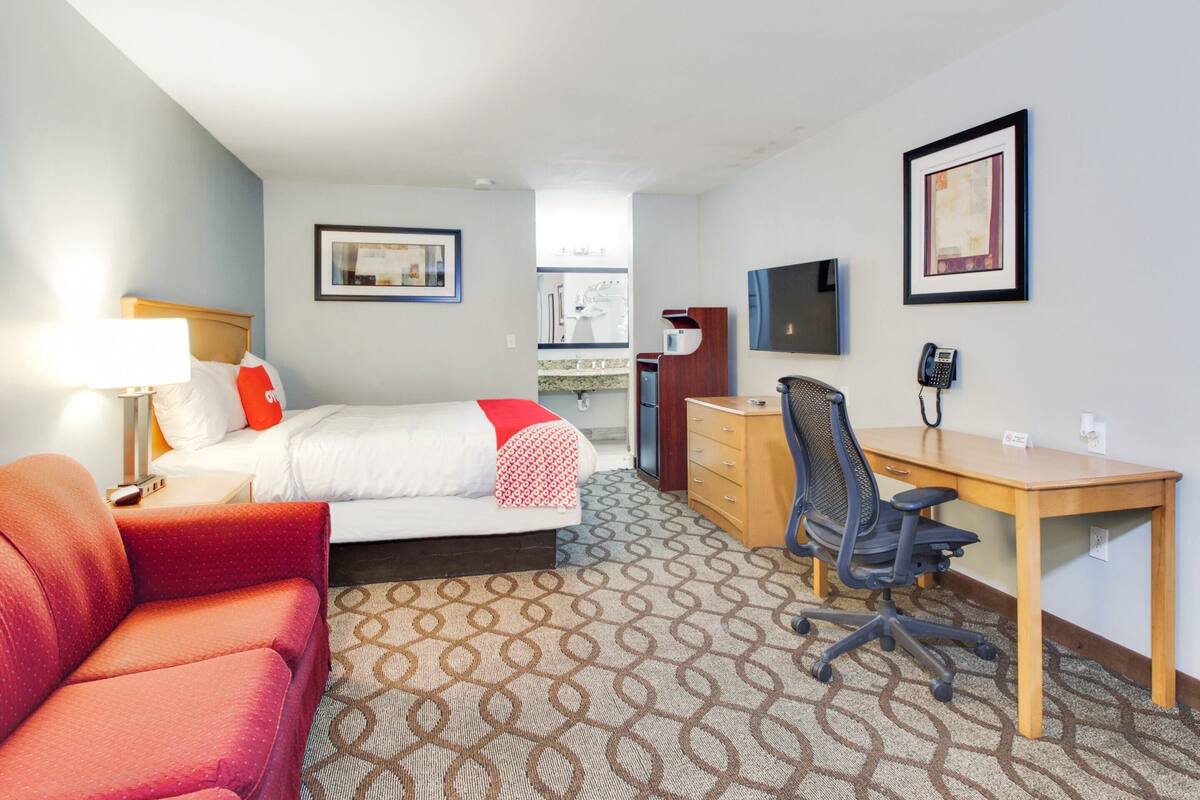 A hotel room with a bed, a desk, a chair, a TV, and a phone.