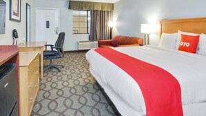 A hotel room with a large bed, a desk, a chair, and a window with curtains.