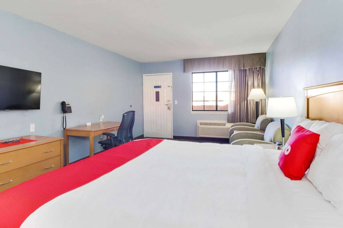 A hotel room with a large bed, a desk, a chair, a TV, a door, and a window.