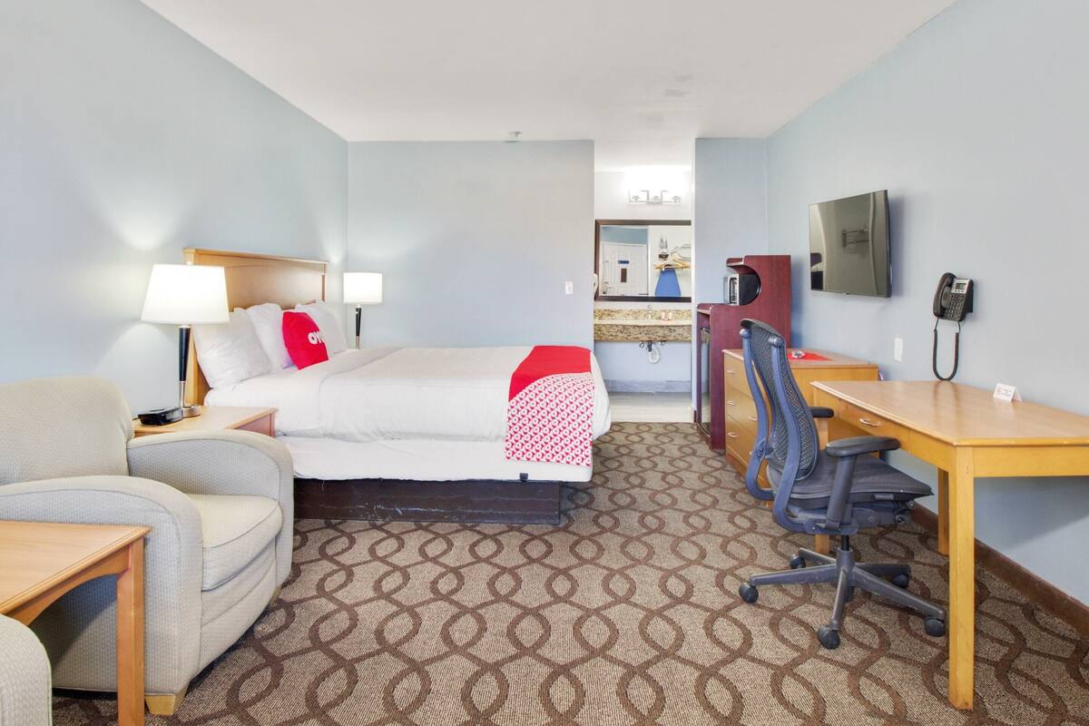 A hotel room with a bed, a desk, a chair, a lamp, a telephone, and a television.