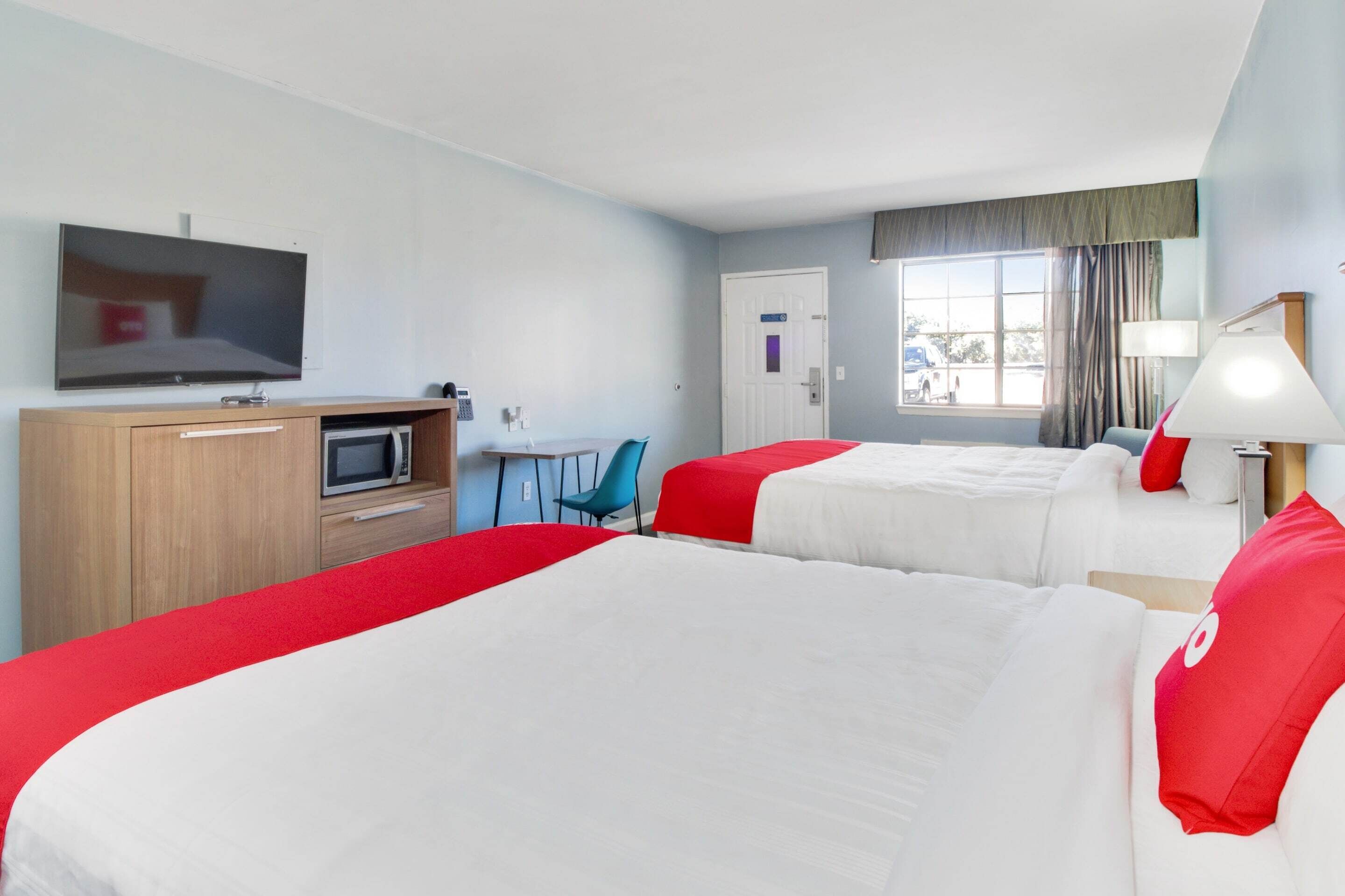 A hotel room with two beds, a TV, a desk, a chair, and a window with curtains.