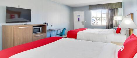 A hotel room with two beds, a TV, a desk, a chair, and a window with curtains.