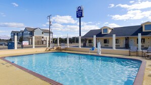 A swimming pool with a lifeguard sign, a hotel sign, and a fenced area with chairs.