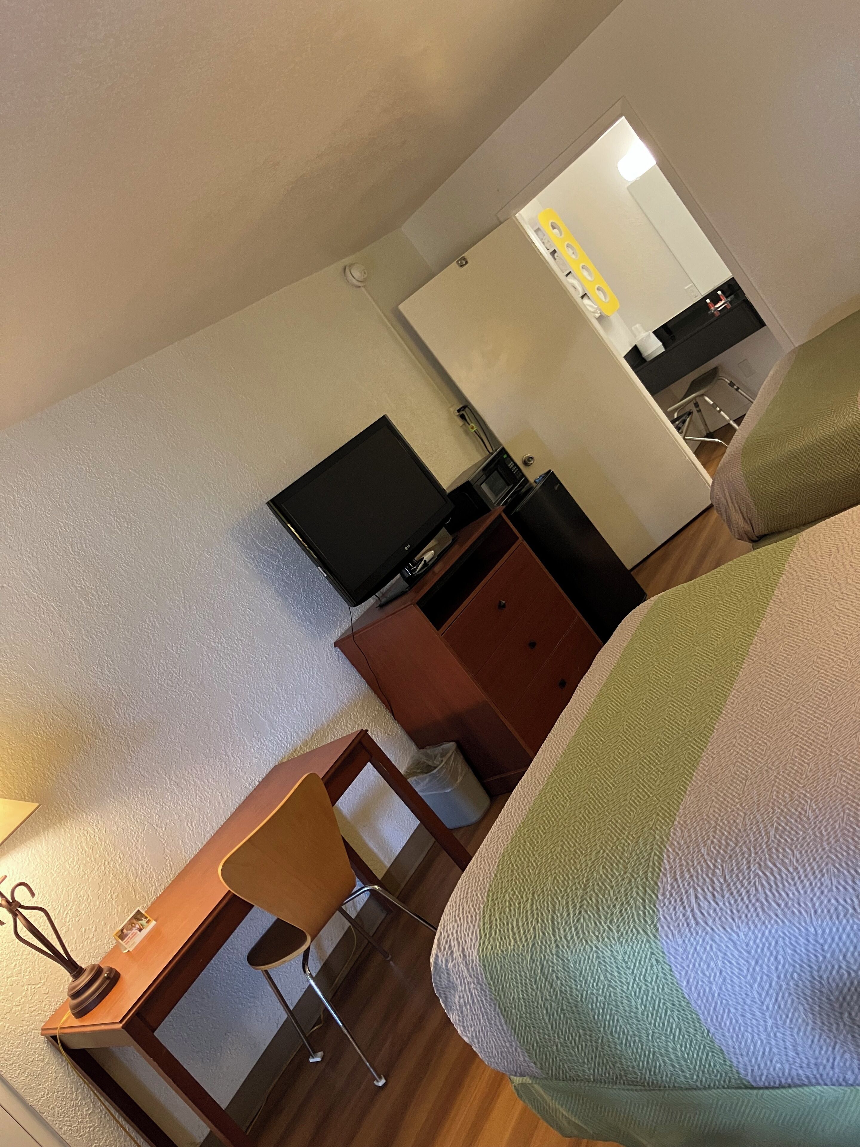 A hotel room with a bed, a desk with a chair, a television, a microwave, and a small kitchenette area.