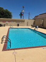 Una piscina rectangular con una escalera metálica en un lado, rodeada por un deck color arena. Hay carteles en la pared que indican servicios e información de seguridad.