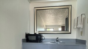 A bathroom with a gray countertop, a sink, a mirror, a towel rack, a trash bin, and a shower curtain rod.