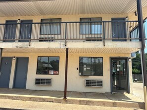 A two-story building with a balcony, a ground-level entrance, and a visible air conditioning unit.