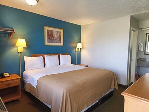 A hotel room with a large bed, two bedside lamps, a painting on the wall, and a wooden nightstand with a phone.