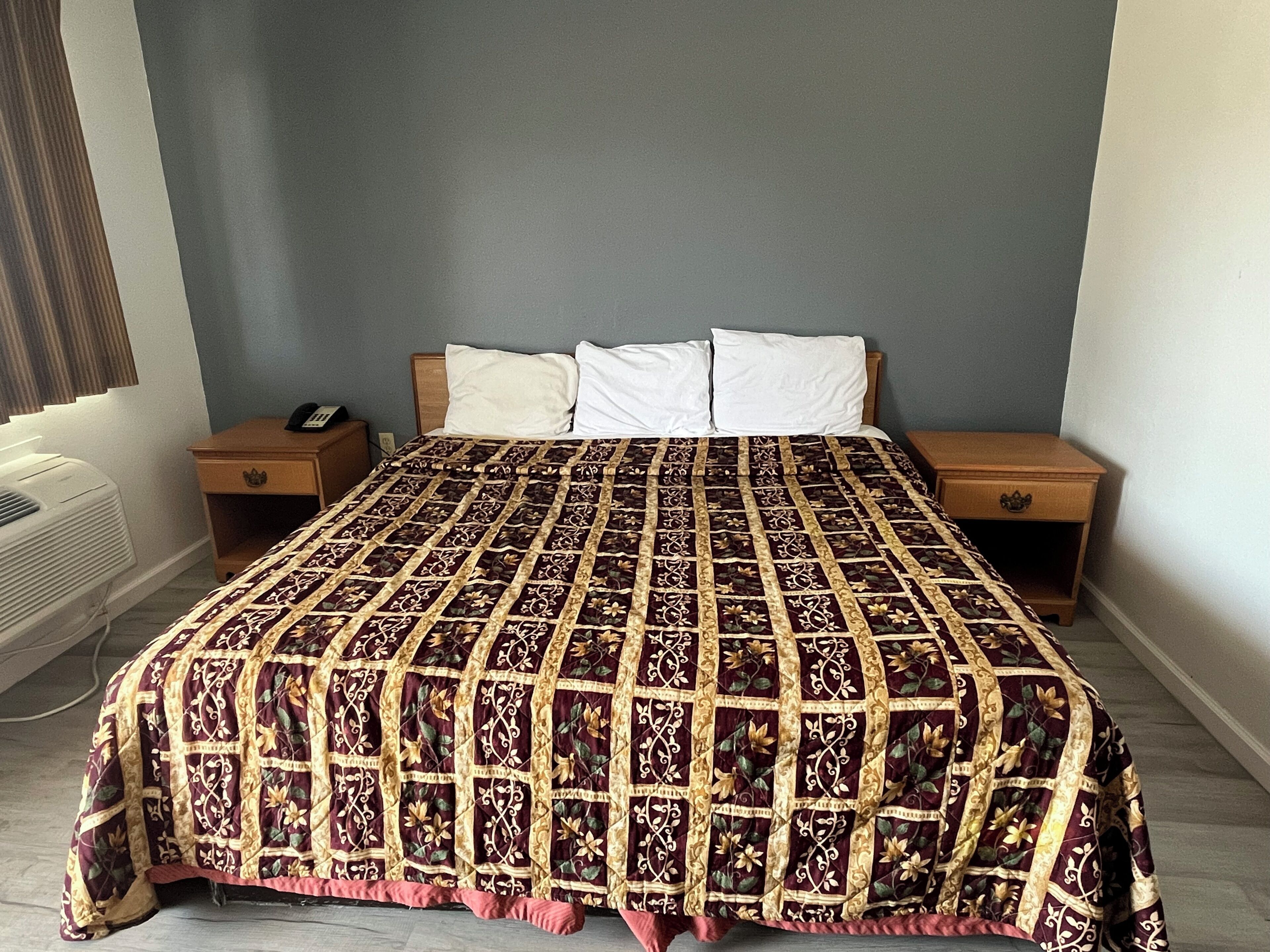 A bed with a patterned bedspread, two bedside tables, a nightstand, and a wall-mounted telephone.