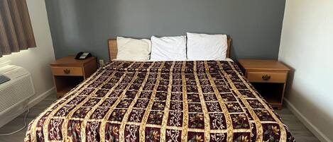 A bed with a patterned bedspread, two bedside tables, a nightstand, and a wall-mounted telephone.