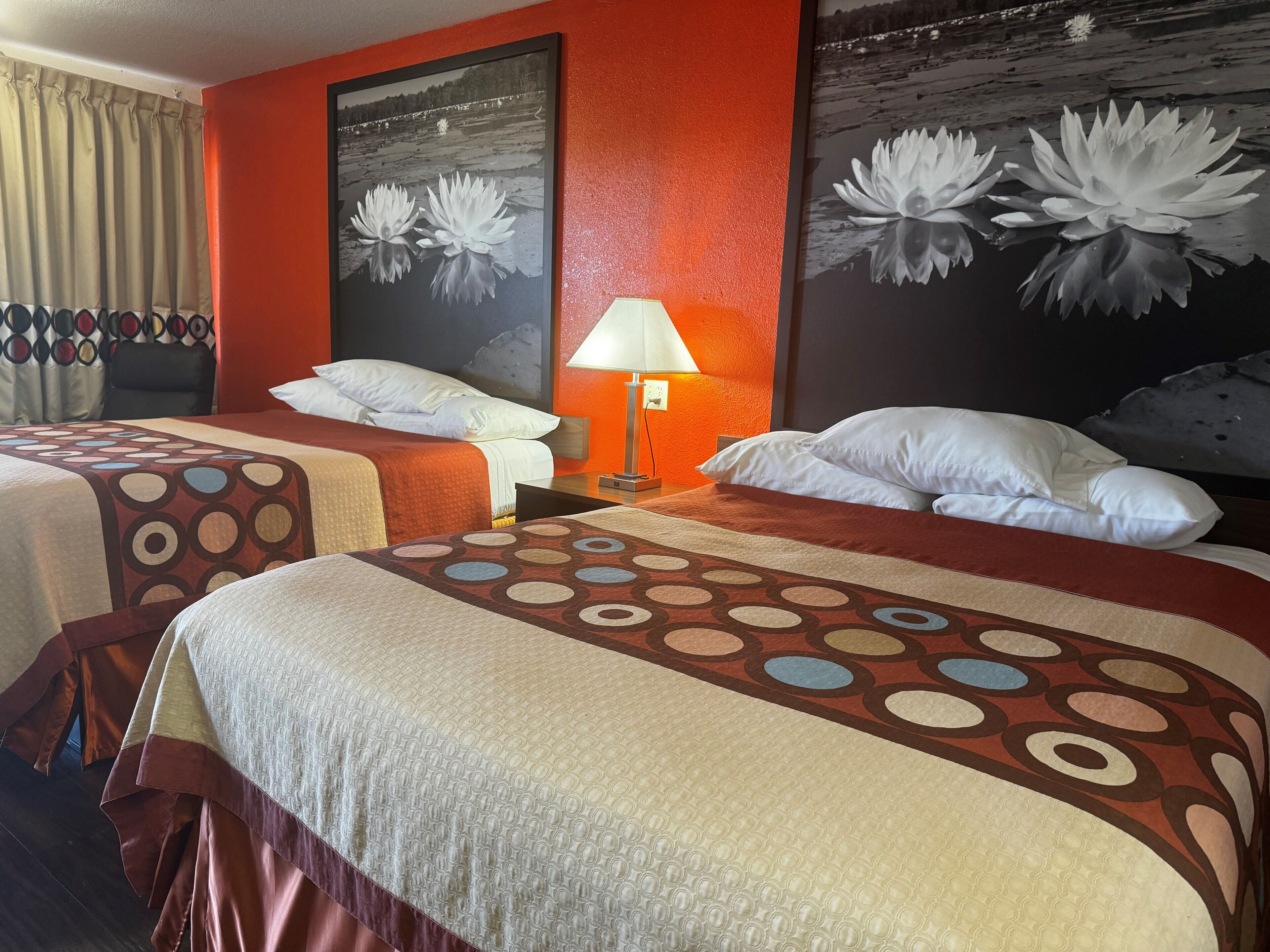 Une chambre d’hôtel avec deux lits, une table de chevet avec une lampe et deux grandes œuvres d’art murales à motifs floraux.