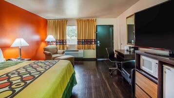 A hotel room with a bed, desk, chair, TV, and kitchenette.