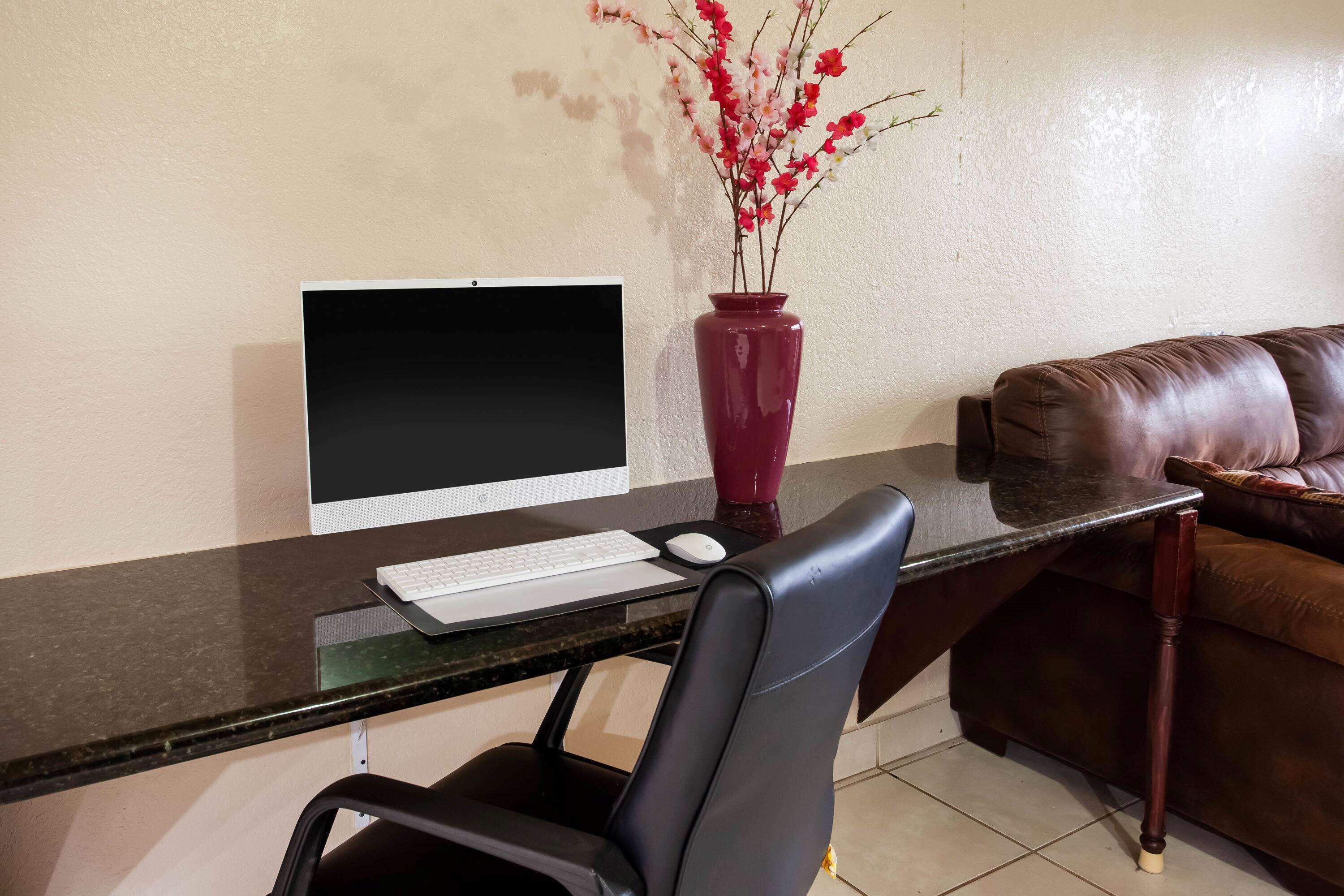A workspace with a computer, keyboard, and mouse on a desk, a chair, a vase with flowers, and a leather couch.