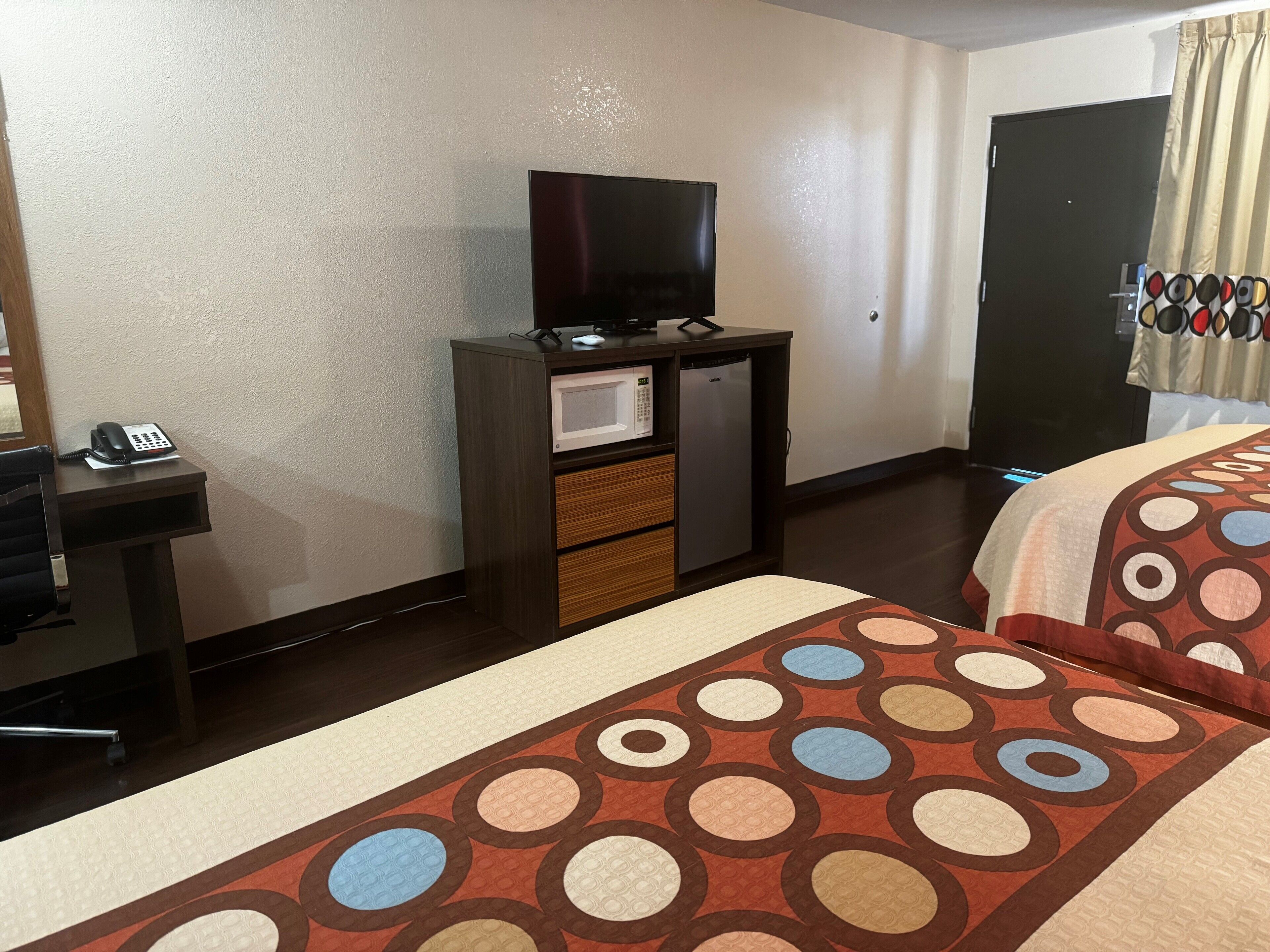 Habitació d'hotel amb llit, escriptori amb telèfon, televisió i nevera minibar.