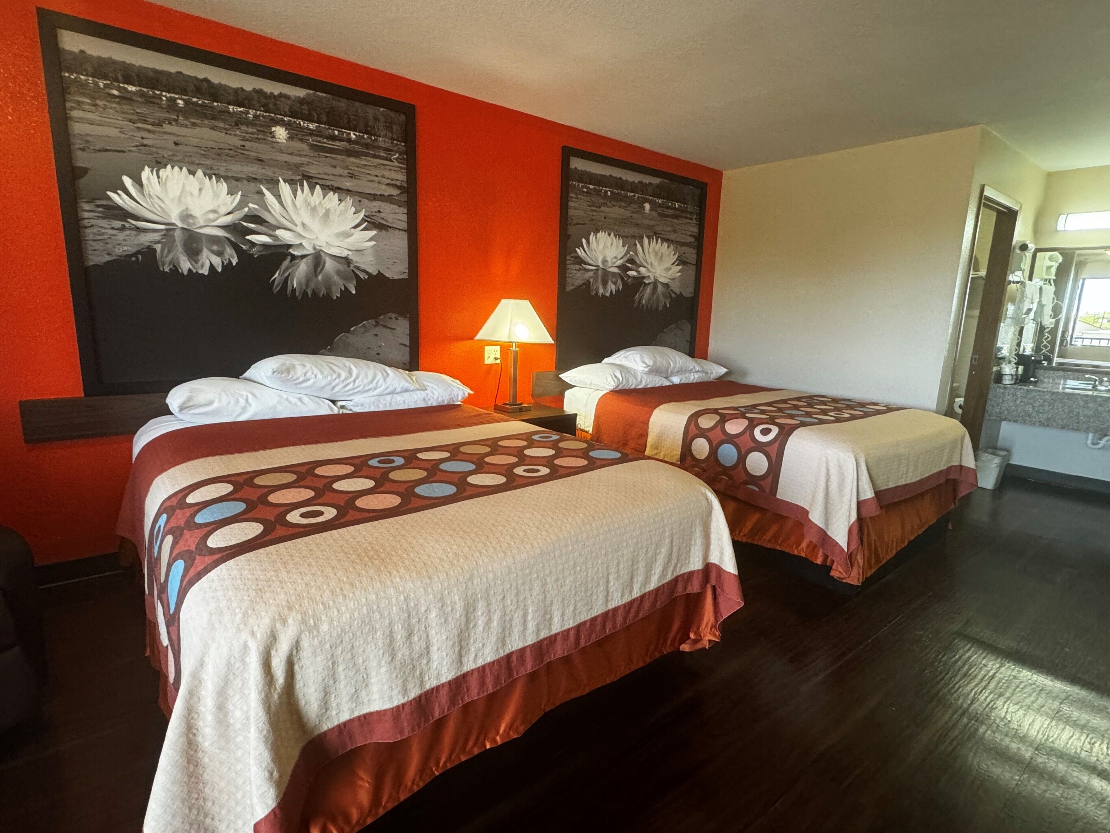 A hotel room with two beds, a nightstand with a lamp, and a bathroom visible through an open door.