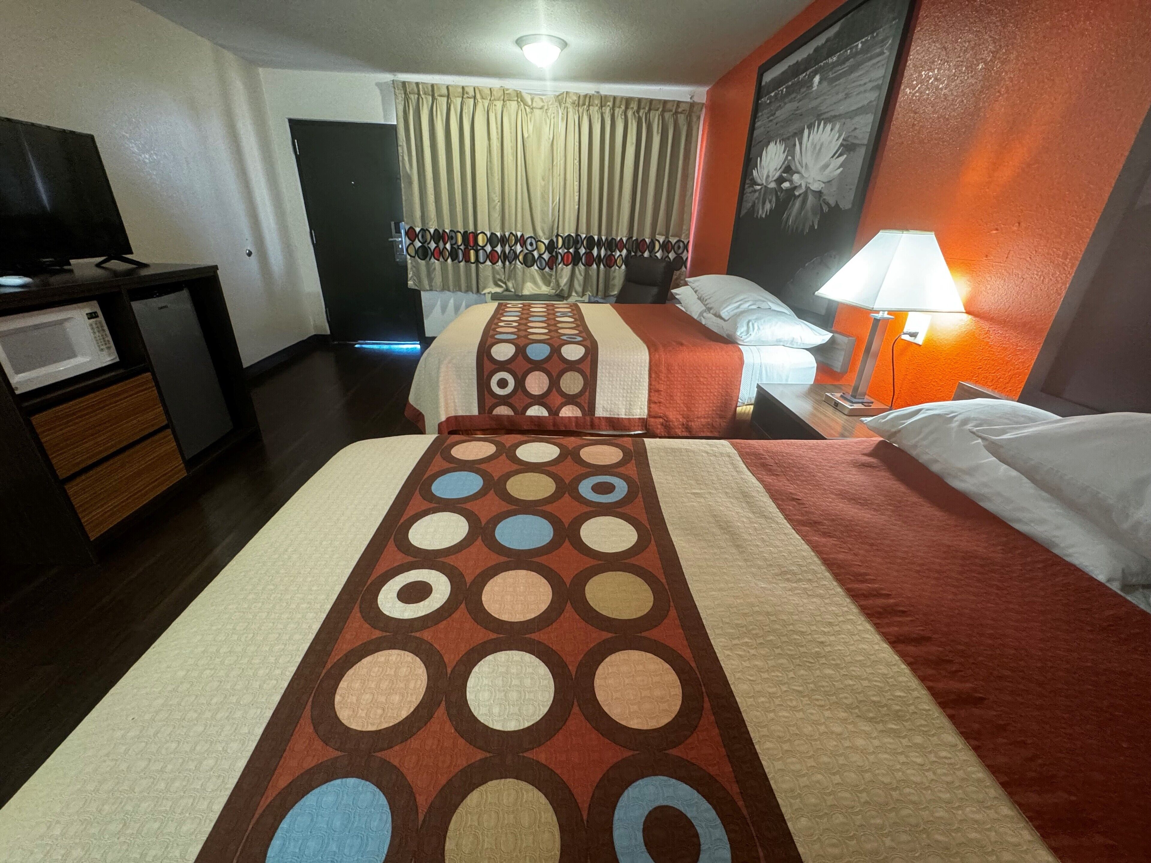 Quarto de hotel com duas camas, uma escrivaninha com micro-ondas e uma mesa de cabeceira com abajur.