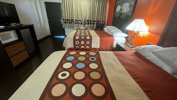 Quarto de hotel com duas camas, uma escrivaninha com micro-ondas e uma mesa de cabeceira com abajur.