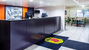 A reception area with a counter, a large poster, and a seating area with tables and chairs. - Super 8 by Wyndham Giddings (Giddings)
