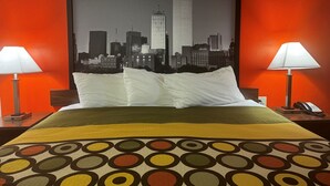 A hotel room with a cityscape view, a bed with white pillows, a patterned throw, and two bedside lamps. - Super 8 by Wyndham Giddings (Giddings)
