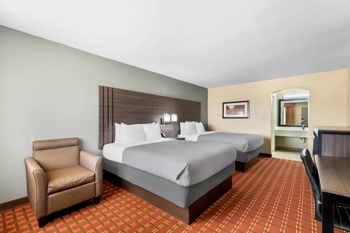 Ein Hotelzimmer mit Bett, zwei Nachttischen, einem Sessel, einem Schreibtisch und einem Spiegel.