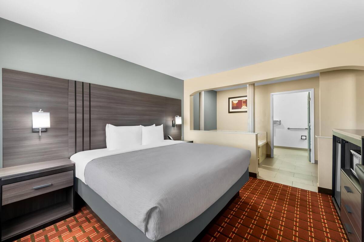 Ein Hotelzimmer mit einem großen Bett, Nachttischen, einem Spiegel und einer Tür zu einem Badezimmer.