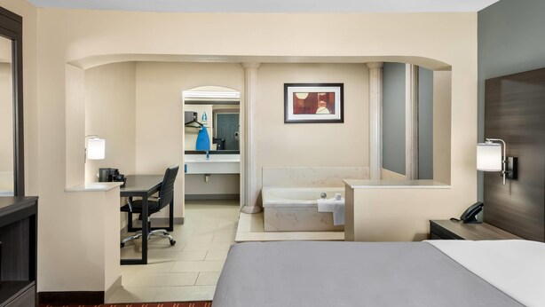 Habitación de hotel con cama, escritorio, silla y baño con bañera y espejo.