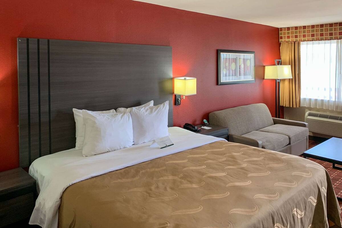 Ein Hotelzimmer mit einem großen Bett, einem Sessel, einem kleinen Tisch und zwei Wandlampen.