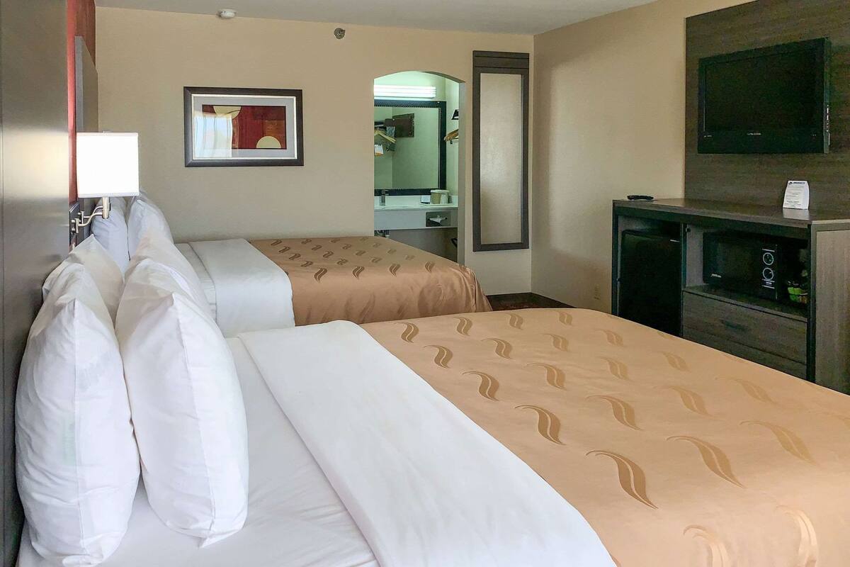 Ein Hotelzimmer mit zwei Betten, einem Fernseher, einem Spiegel und einem Schreibtisch mit Lampe.