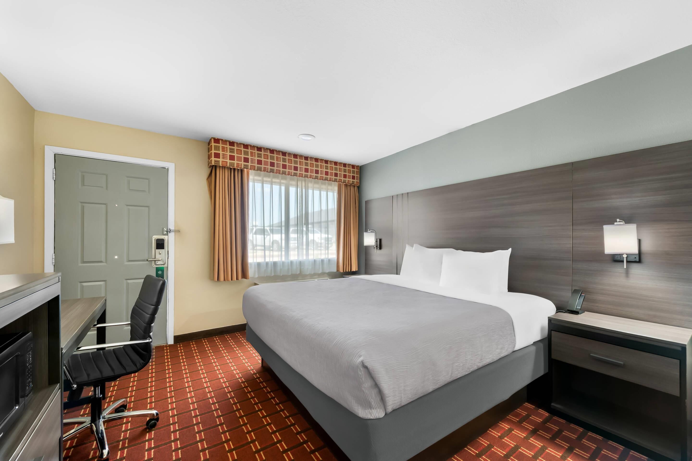 Una habitación de hotel con cama, escritorio, silla y ventana con cortinas.