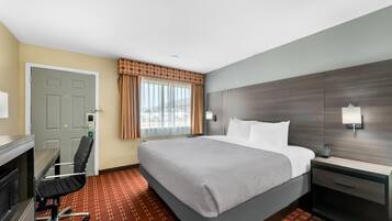 Una habitación de hotel con cama, escritorio, silla y ventana con cortinas.
