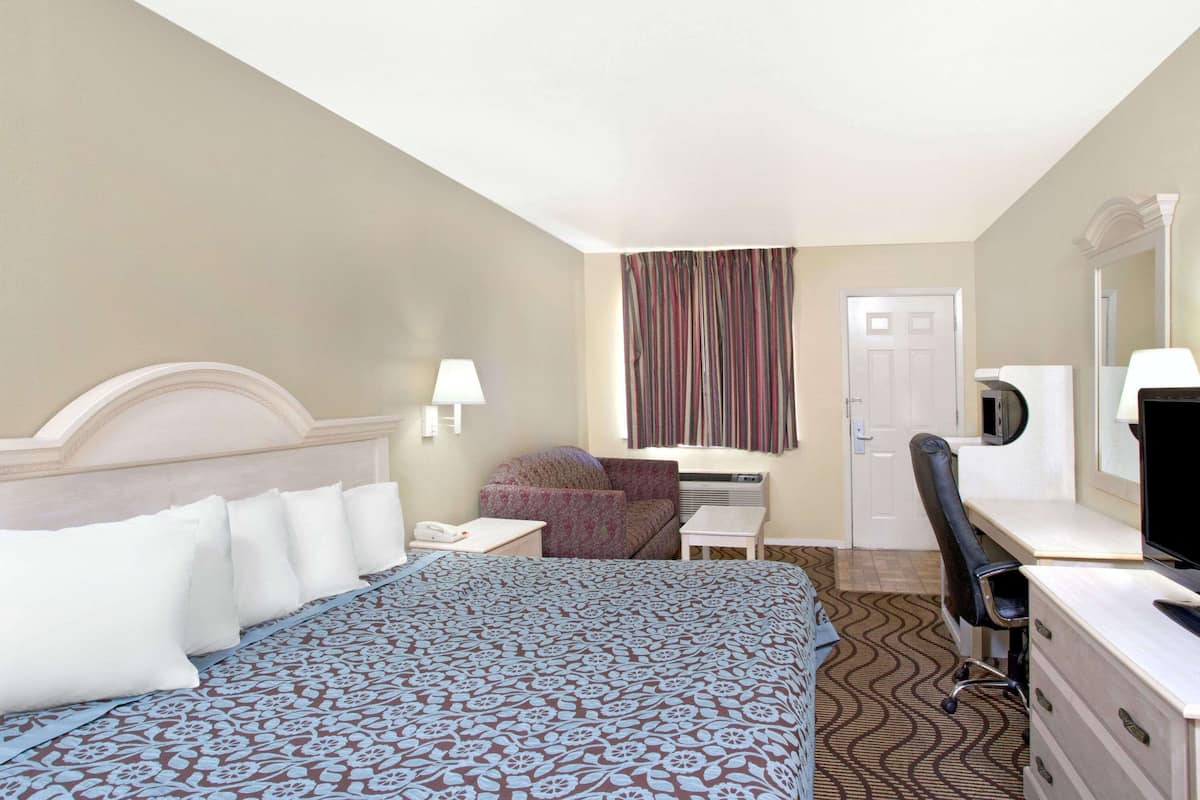 Ein Hotelzimmer mit einem Bett, einem Schreibtisch, einem Sessel, einem Fernseher und einer Tür.