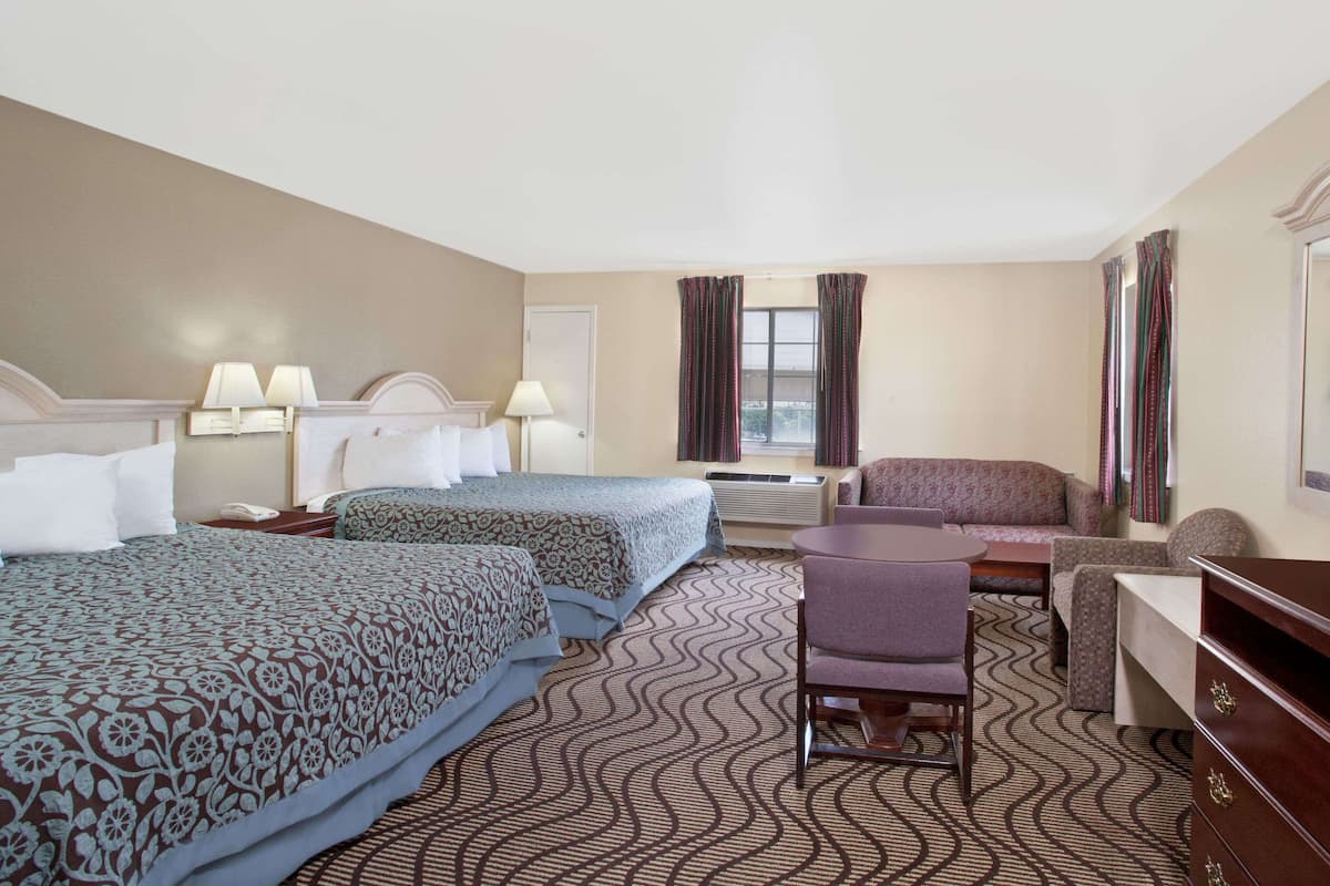 Ein Hotelzimmer mit zwei Betten, einem Sofa, einem Sessel, einem Schreibtisch und einem Fenster mit Vorhängen.