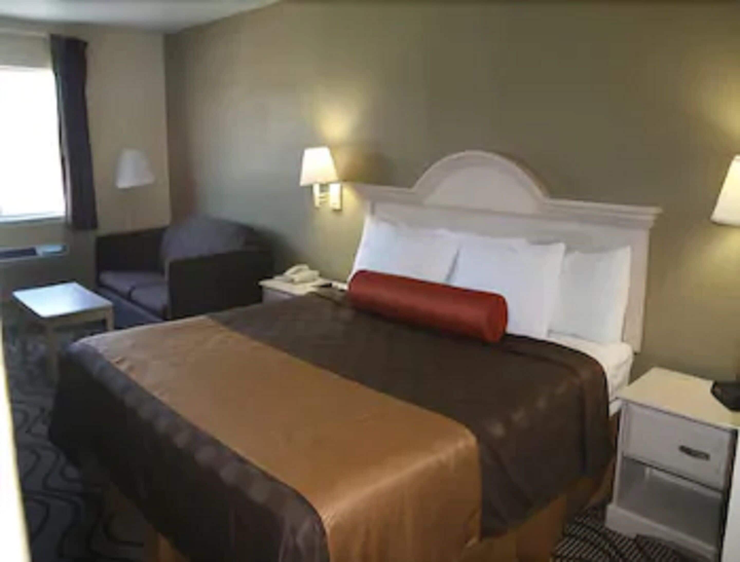 A hotel room with a large bed, a nightstand, a lamp, and a chair.