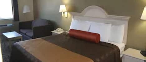 A hotel room with a large bed, a nightstand, a lamp, and a chair.