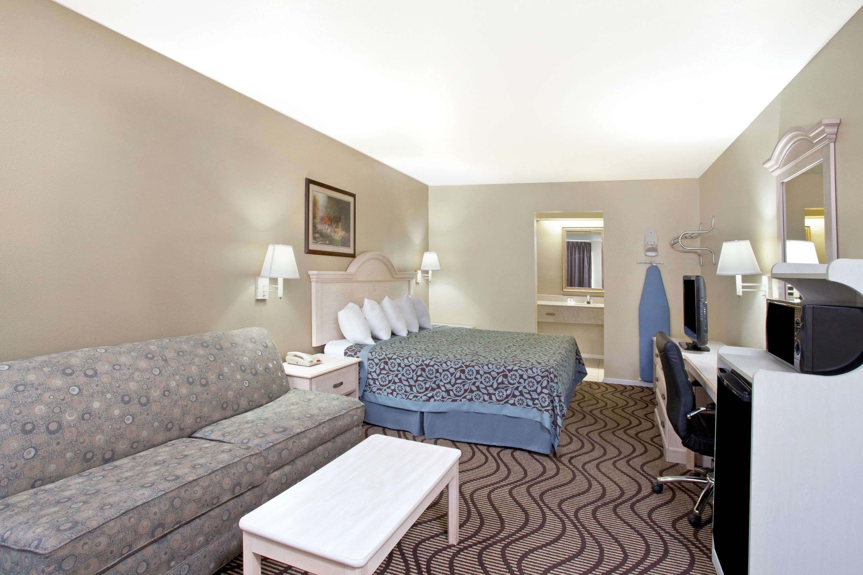 A hotel room with a bed, a sofa, a desk, and a mirror.