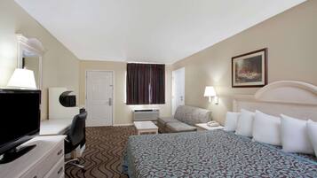 Une chambre d’hôtel avec un lit, un bureau avec une télévision, une chaise, une petite table, une lampe et un tableau au mur.