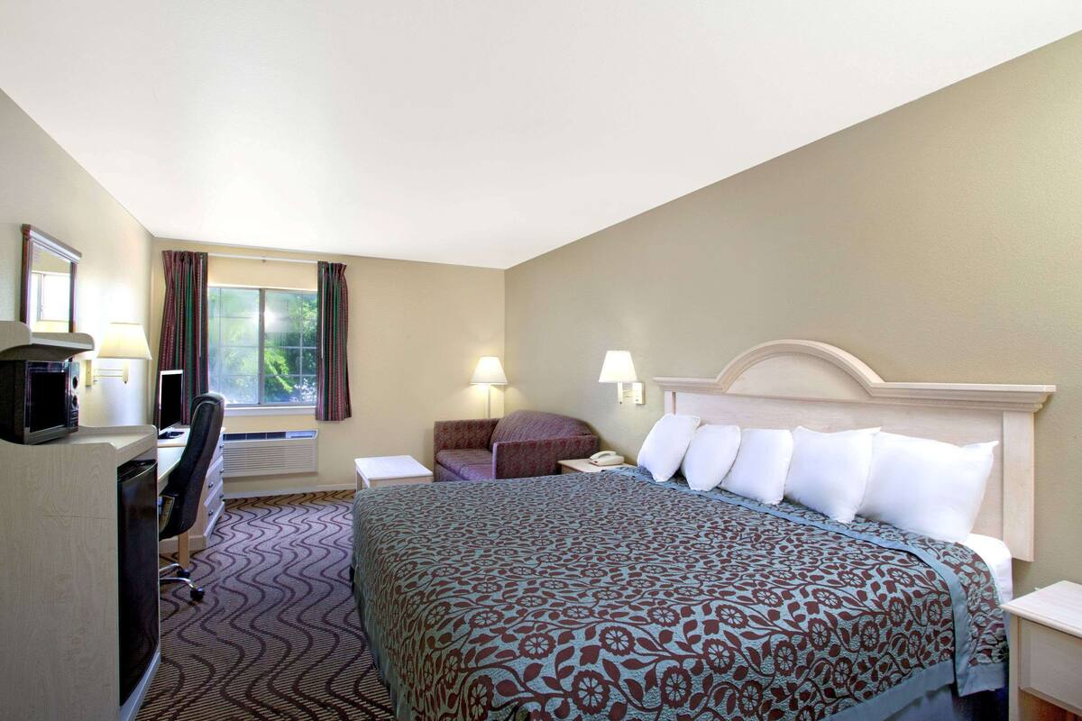 Ein Hotelzimmer mit Bett, Schreibtisch, Stuhl und einem Vorhangfenster.