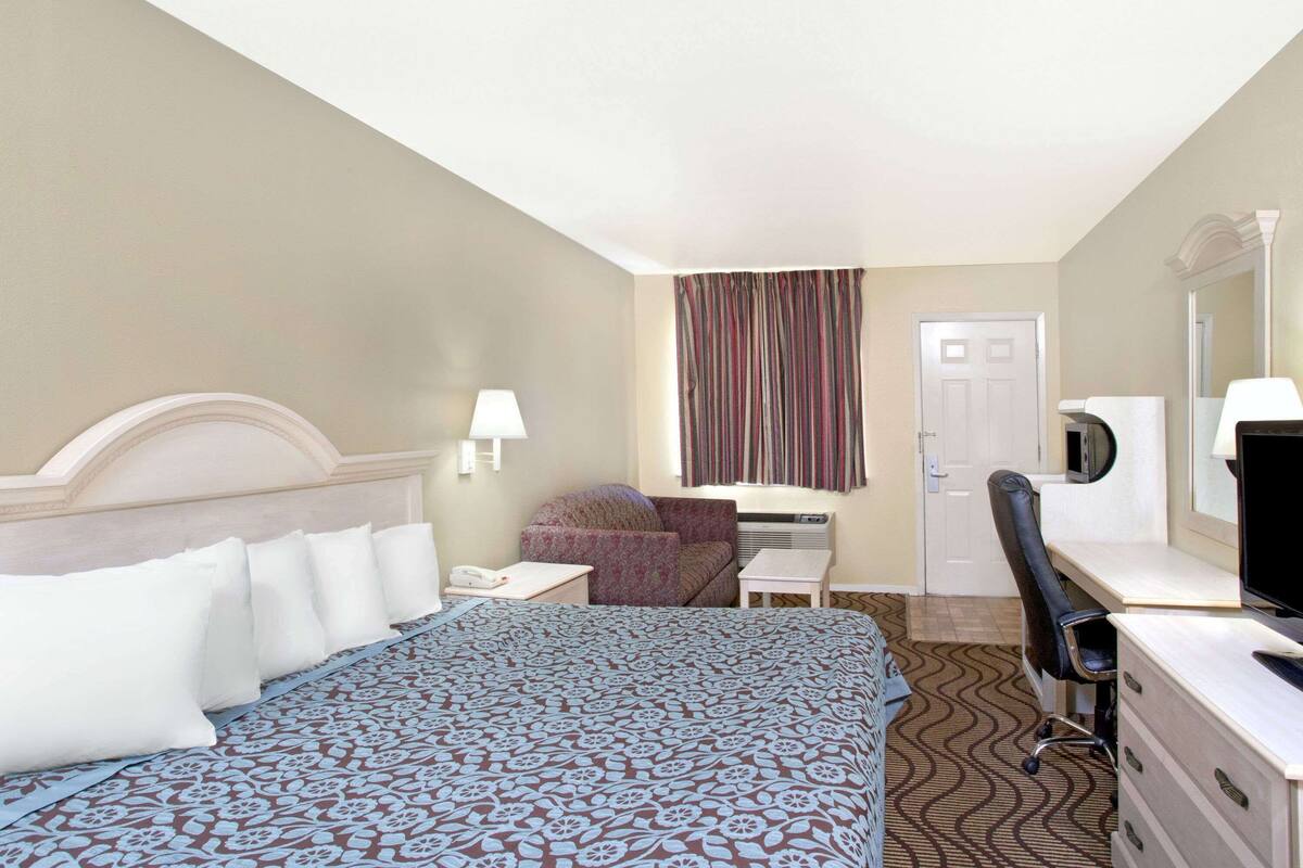 Ein Hotelzimmer mit Bett, Schreibtisch, Stuhl, Fernseher und Tür.